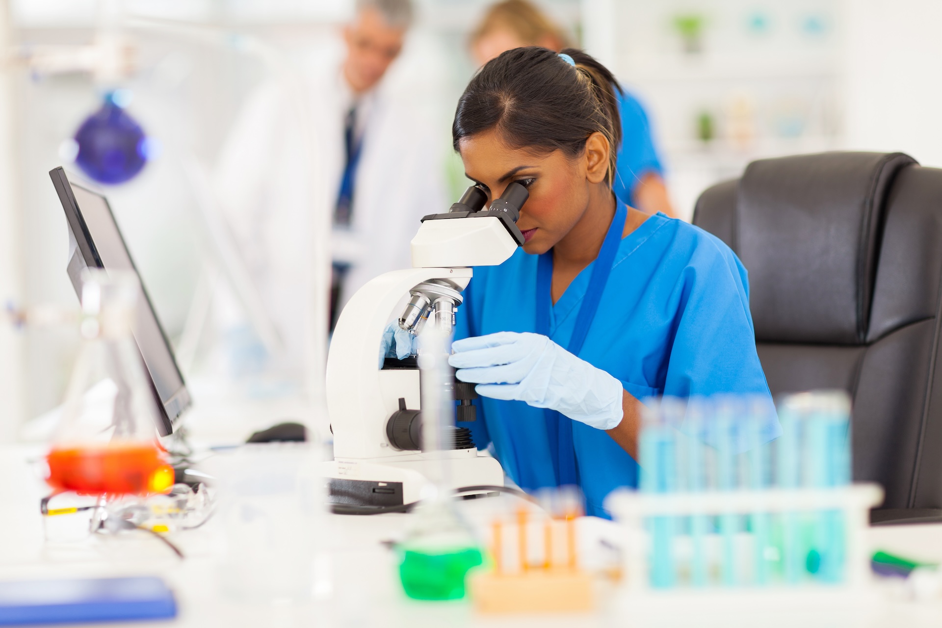 young indian medical researcher looking through microscope in laboratory