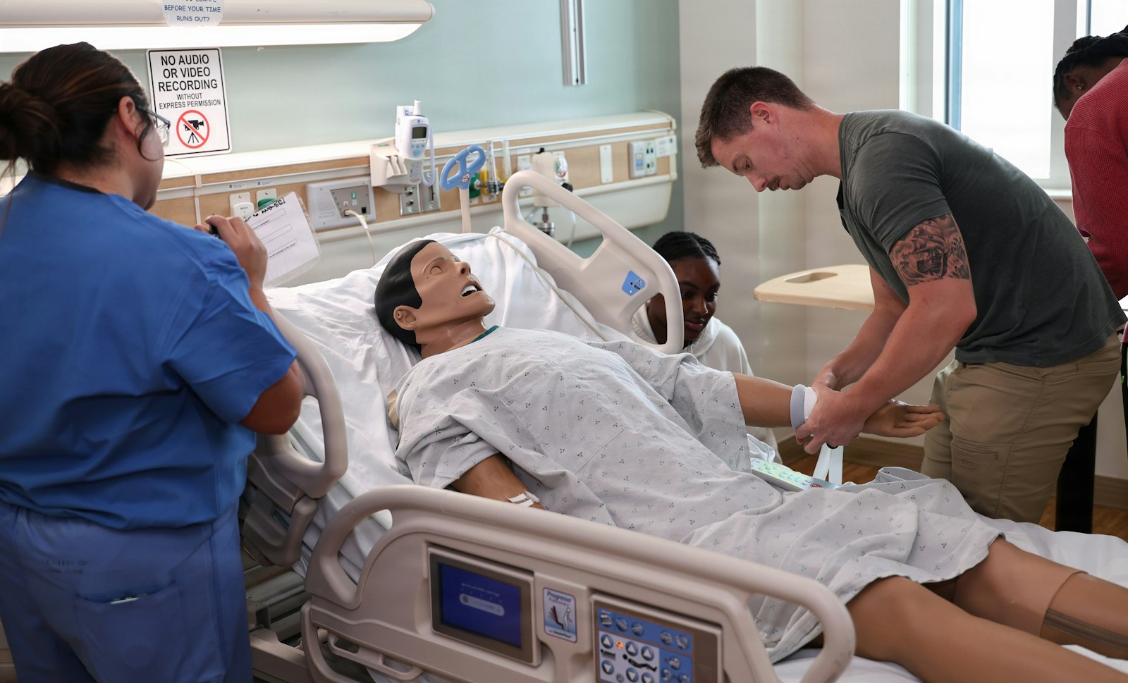 Healthcare students in scrubs practicing patient care skills on a simulation mannequin